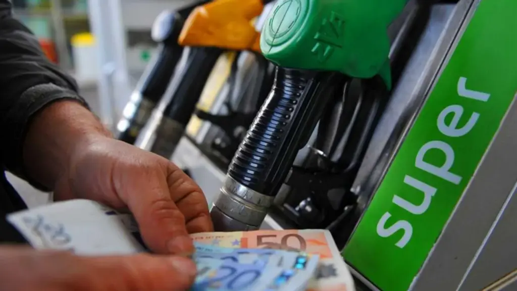 Pompa di benzina con due mani che mostrano soldi per rappresentare gli extraprofitti delle società energetiche