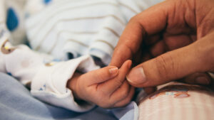 Mano di una mamma che accarezza la mano di un neonato, simbolo del crollo delle nascite nel I Municipio di Roma